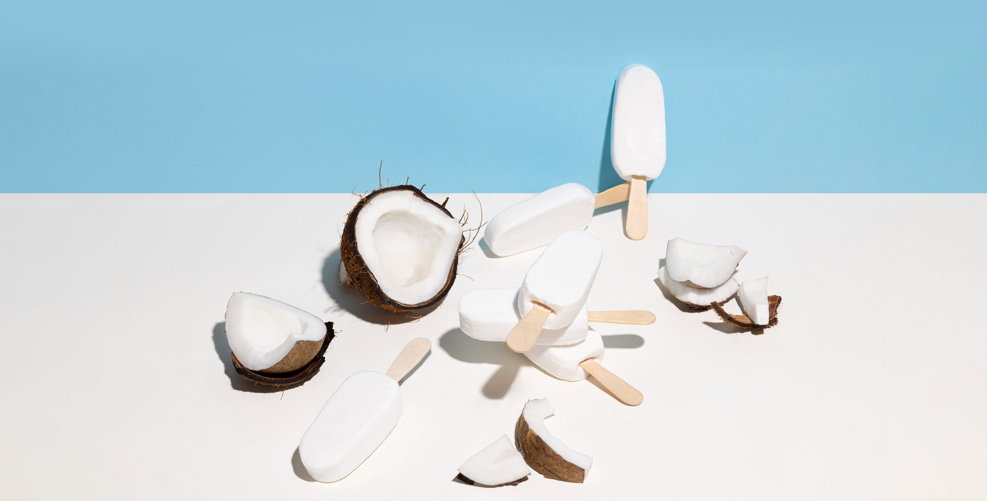 Coconut halves and ice cream popsicles on a white surface with a blue background