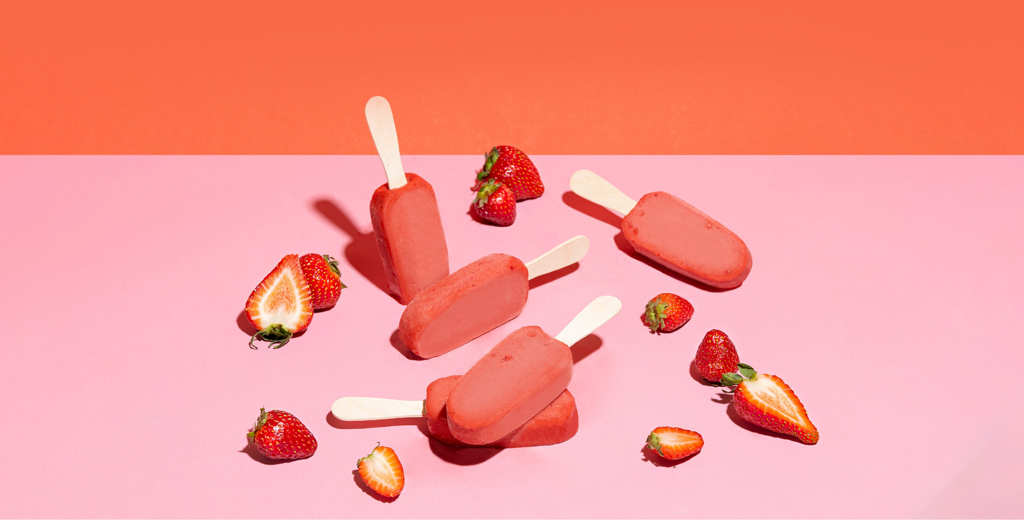 Strawberry popsicles and strawberries on a pink and orange gradient background