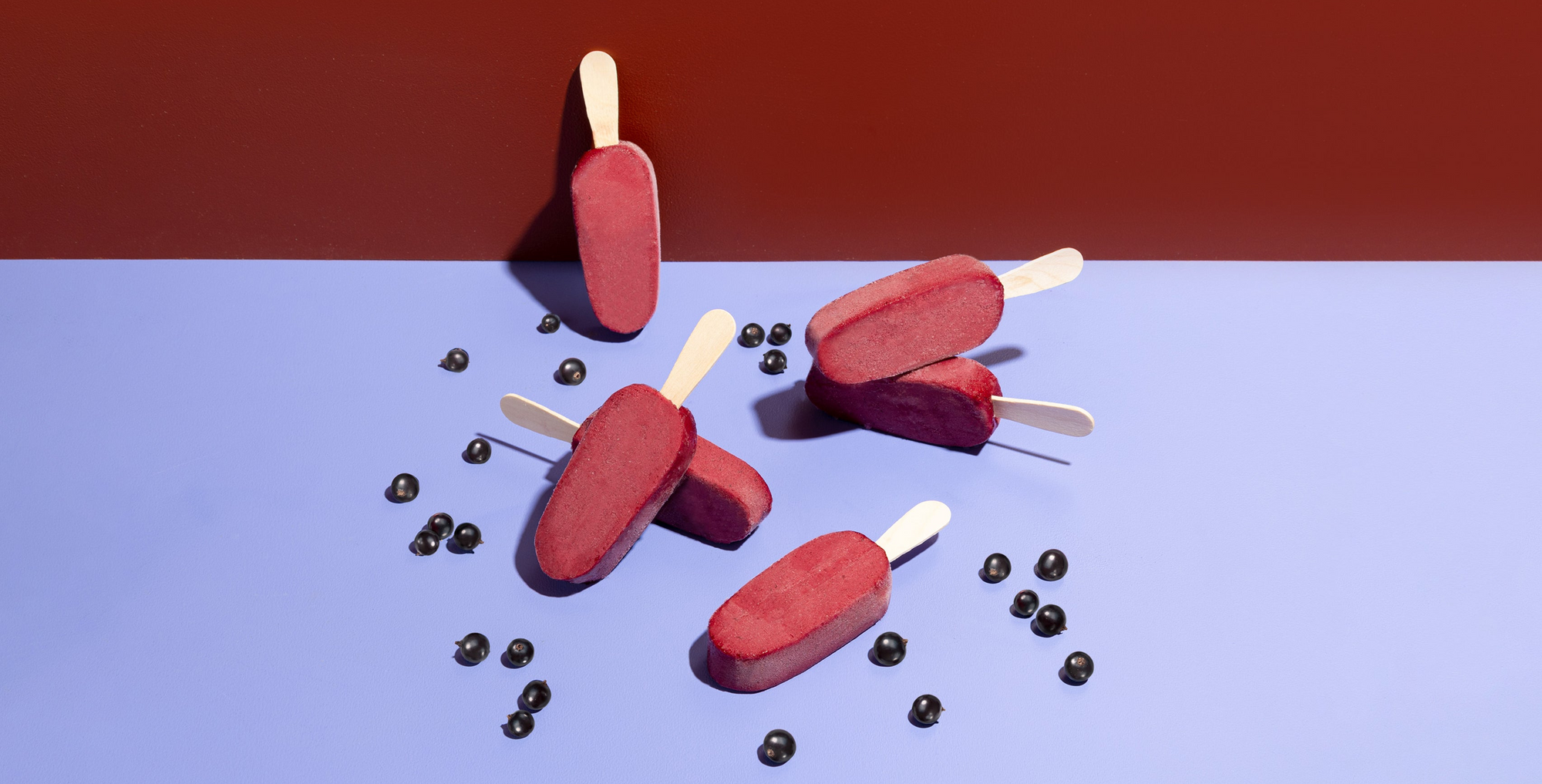 Red popsicles on a blue surface with black currants