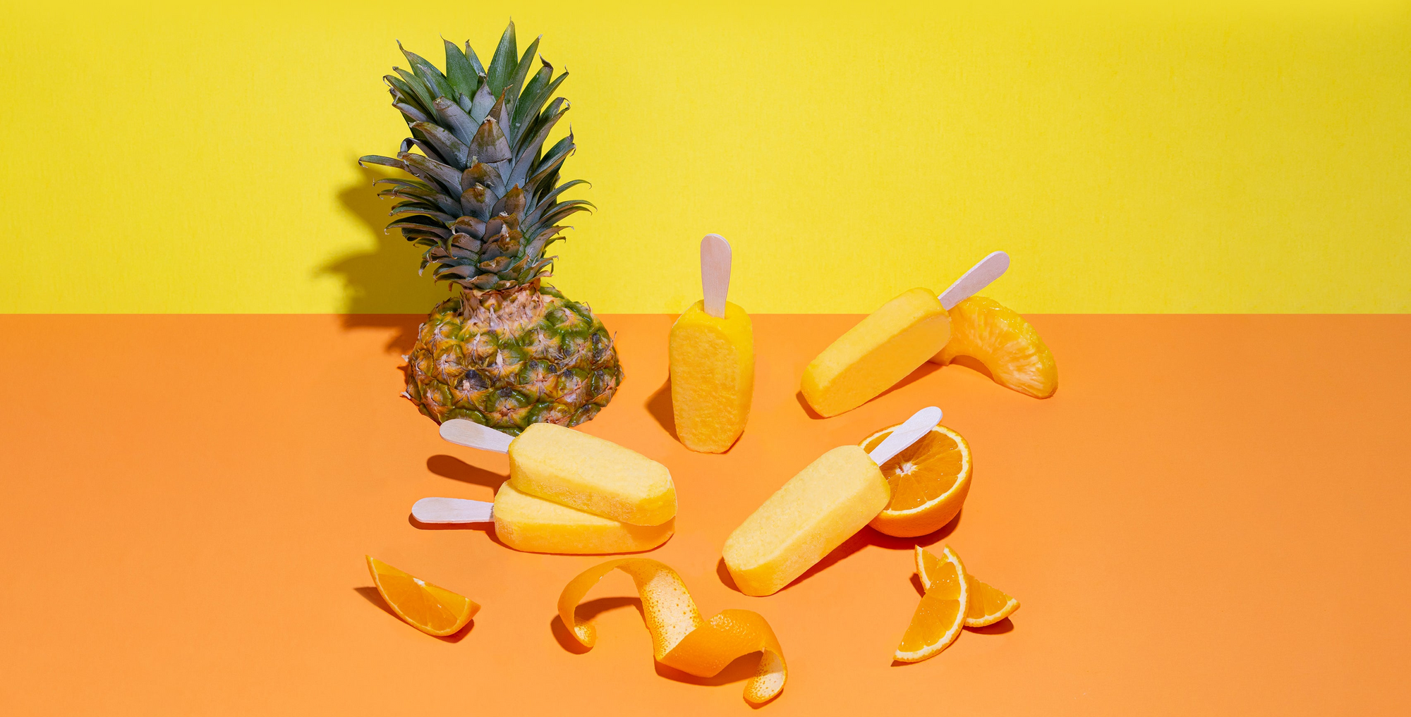 Pineapple and orange popsicles on a yellow and orange gradient background